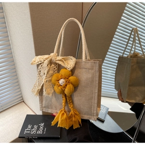 Dettaglio borsa in lino con fiocco di pizzo e ciondolo a fiore in peluche giallo