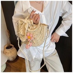 Détail du sac seau en paille avec nœud en dentelle et breloques de fleurs au crochet