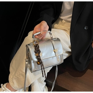 Detail view of silver metallic bag with gold circular buckle and woven rope charm
