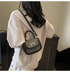 Polka dot saddle bag with silver bow accent worn as a crossbody by a model in a minimalist room