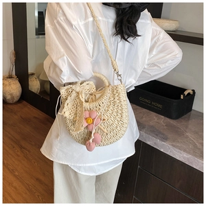 Détail d'un sac seau en paille avec nœud en dentelle délicat et breloques florales