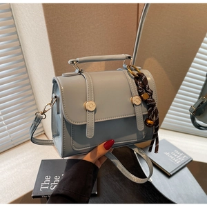 Detail of light blue faux leather satchel with gold buckles and woven tassel charm