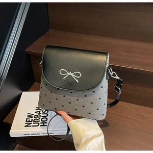 Detail of grey canvas bucket bag with heart prints and silver metal bow on black flap