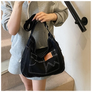Detail shot of black denim tote with white contrast stitching and leather brand patch