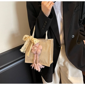 Dettaglio della borsa in iuta con fiocco in pizzo bianco e ciondolo a fiore rosa