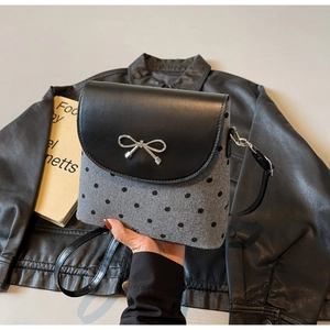 Detail of grey polka dot crossbody bag with black leather flap and silver bow buckle