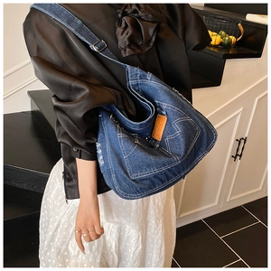 Close-up of vintage blue denim tote bag featuring white stitching and brown leather patch