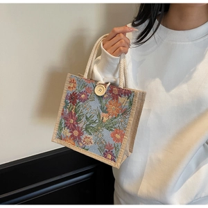 Detail of floral linen tote bag featuring thick rope handles and wooden button closure