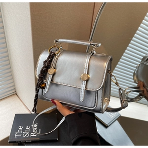 Detail of silver metallic crossbody bag featuring gold hardware and a woven lanyard charm