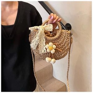 Détail du sac bandoulière en paille avec nœud en dentelle blanche et pendentif fleur