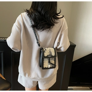 Detail of a black leather crossbody bag with beige floral print flap and slim strap
