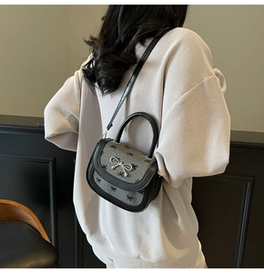 Fashionable grey bow saddle bag with silver buckle worn by model against dark wall