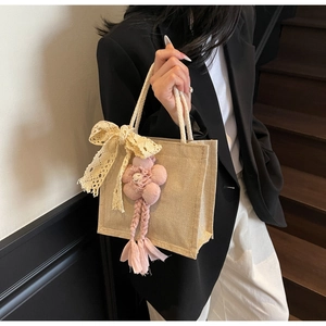 Dettaglio della borsa in iuta con fiocco in pizzo beige e ciondolo a fiore di peluche