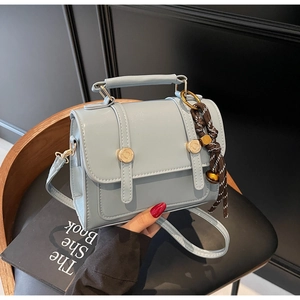Close-up of light blue leather crossbody bag with gold round clasp and woven rope charm