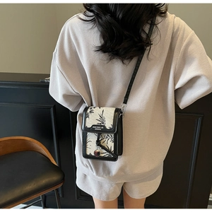 Detail of a chic monochrome printed crossbody bag with a round metal pendant and leaf texture