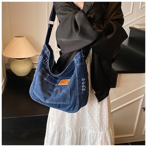 Detail of blue denim tote bag featuring adjustable strap and leather sports tag