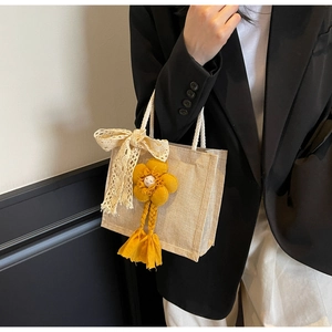 Dettaglio borsa in lino con ciondolo a girasole giallo e fiocco in pizzo bianco
