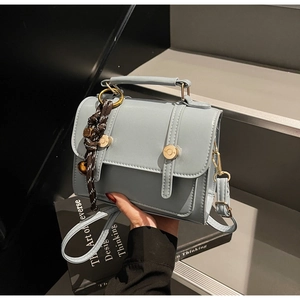Detail view of a light blue-grey square crossbody bag with gold magnetic buckle closure