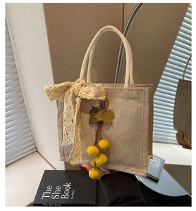 Detail of beige woven lunch bag featuring lace bow and green leaf pendant accessory