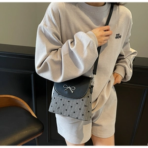 Close-up of a grey polka dot crossbody bag with a silver bow and black leather flap