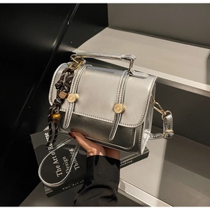 Detail of silver metallic square handbag with gold buckles on modern urban stairs