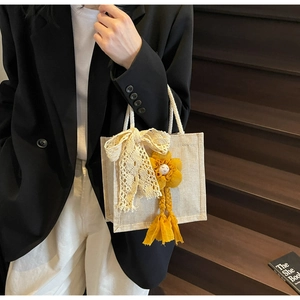 Dettaglio borsa in tela beige con manici in corda di canapa e ciondolo a fiocco in pizzo