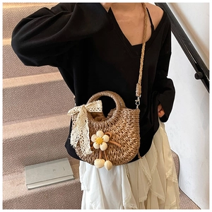 Détail du sac seau en paille avec nœud en dentelle, breloques fleuries et bandoulière