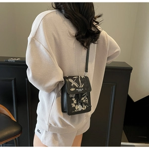 Detail of a black crossbody bag featuring floral embroidery worn by a model in a casual outfit