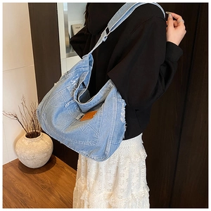Model wearing large denim tote bag with washed fabric and distressed frayed edges