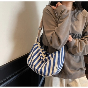 Vue latérale du sac hobo en toile à rayures bleues et blanches porté par le modèle