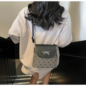 Detail of grey polka dot crossbody bag with black leather flap and silver bow accent