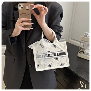 Detail of white tote bag with black rose embroidery, fashion text, and lace scarf