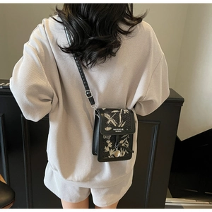 Rear view of a black crossbody phone bag with leaf-textured flap worn over a grey sweatshirt