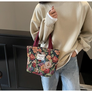 Détail d'un sac cabas en brocart fleuri avec anses bordeaux porté par un mannequin