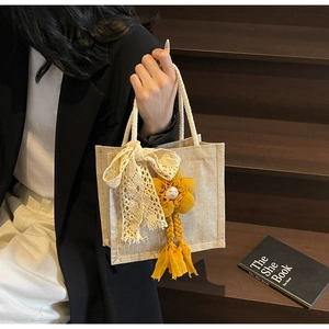 Dettaglio della borsa tote in tela beige con fiocco in pizzo e ciondolo a fiore giallo