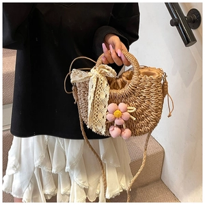Détail du sac seau en paille avec nœud en dentelle crème et breloque fleurie rose