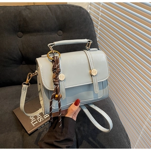 Close-up of light blue handbag with metal handle and woven charm on a grey sofa