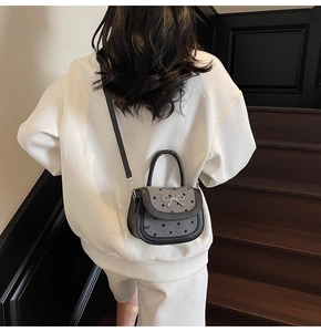 Detail of a mini saddle bag with silver bow and black polka dots on white hoodie