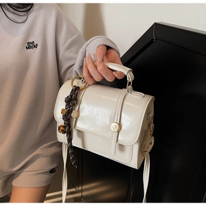 Detail of cream white glossy leather square bag featuring gold hardware and woven rope charm