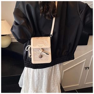 Detail view of beige crossbody phone bag featuring leaf print and pearl charm accent