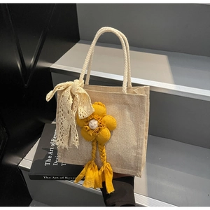 Dettaglio della borsa tessuta beige con fiocco in pizzo bianco e girasole giallo con nappe