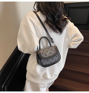 Detailed view of polka dot saddle bag with silver bow accent on model in white clothes