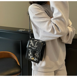 Detail of a mini crossbody phone bag featuring black leather and floral fabric panels