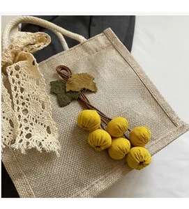 Close-up of linen tote bag with yellow floral pom-poms and cream lace bow detail