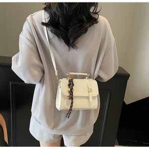Detail showing creamy white crossbody bag with decorative brown twisted rope charm