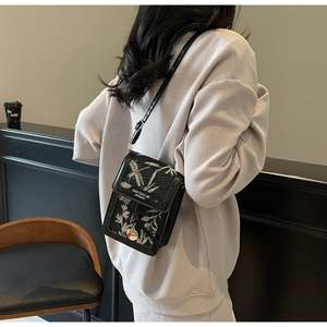 Detailed shot of black leather square bag featuring elegant beige floral embroidery patterns