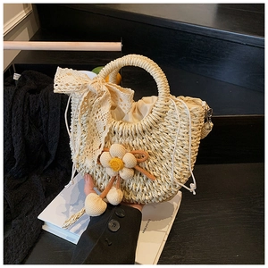 Détail du sac seau en paille avec nœud en dentelle, breloques fleuries et pochette interne