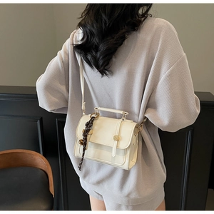 Close-up of a vintage beige crossbody bag featuring a woven charm and metal buckle detail