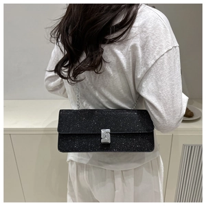 Detail of a black glitter crossbody bag with a silver chain and metal lock on a white dress