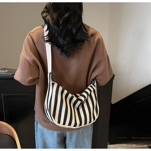 Détail d'un sac bandoulière en toile à rayures noires et blanches porté par un mannequin
